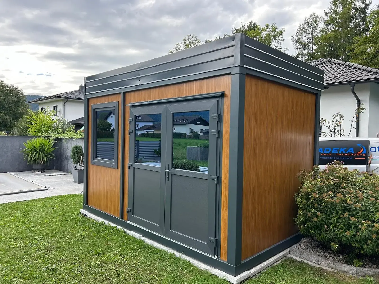 Container da giardino accanto alla siepe e al vialetto pavimentato