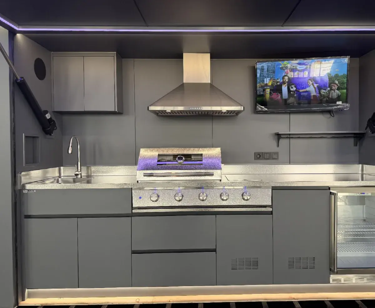 Interno della cucina da esterno con cappa, barbecue, lavello e TV